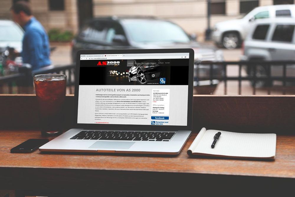 AS200 Webseite auf einem Laptop vor einem Fenster, im Hintergrund sind Auto zu sehen
