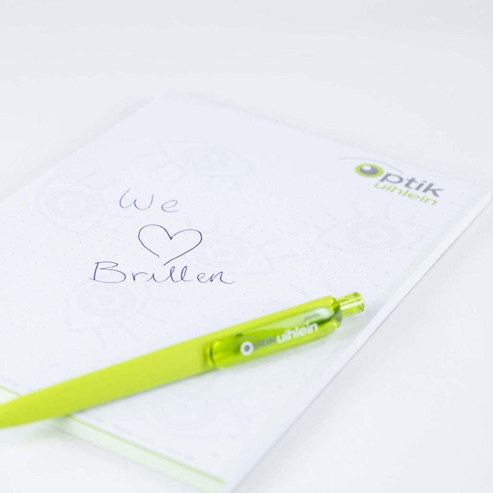 Grüne Kugelschreiber und Blöcke mit Aufschrift "We love Brillen"